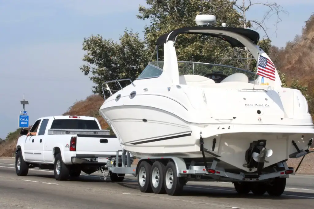 image of a truck towing a tri-axle trailer with a cabin cruiser down the highway.